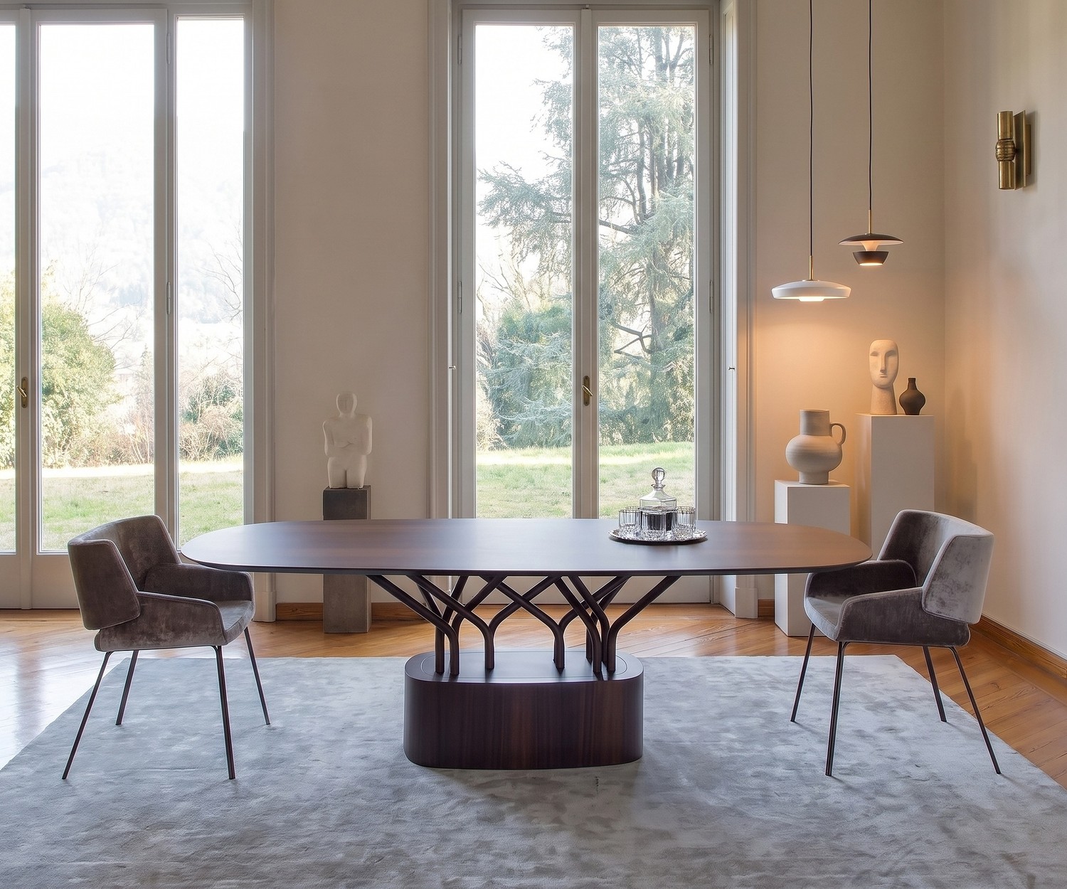 al2 wood-oo ovale design eettafel Ovale al2 wood-oo houten eettafel in een moderne eetkamer met twee grijze fluwelen stoelen en grote ramen.