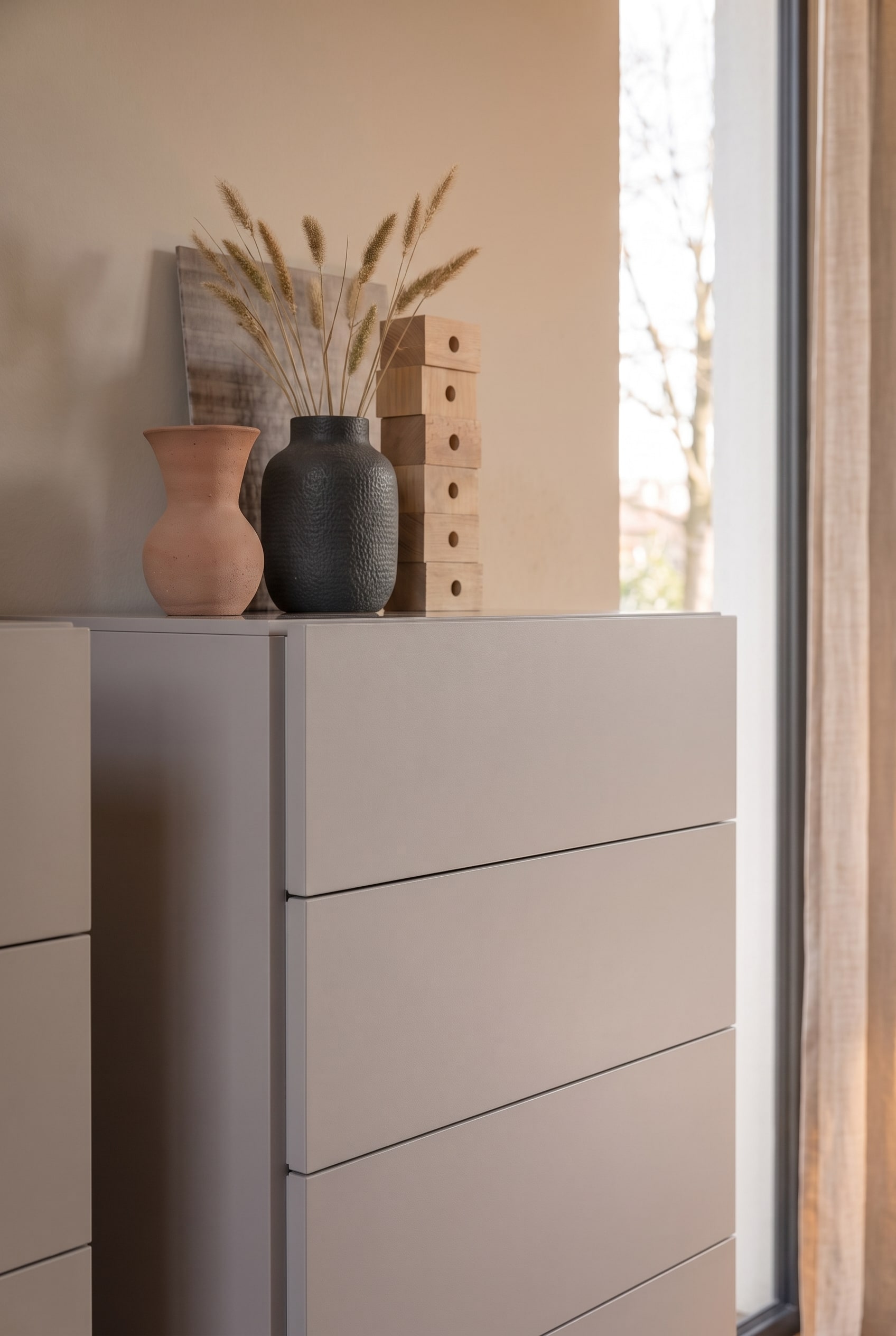 Nahaufnahme einer greigen Kommode, dekoriert mit Terrakotta-Vasen, dunkler Keramik und getrockneten Gr&auml;sern.