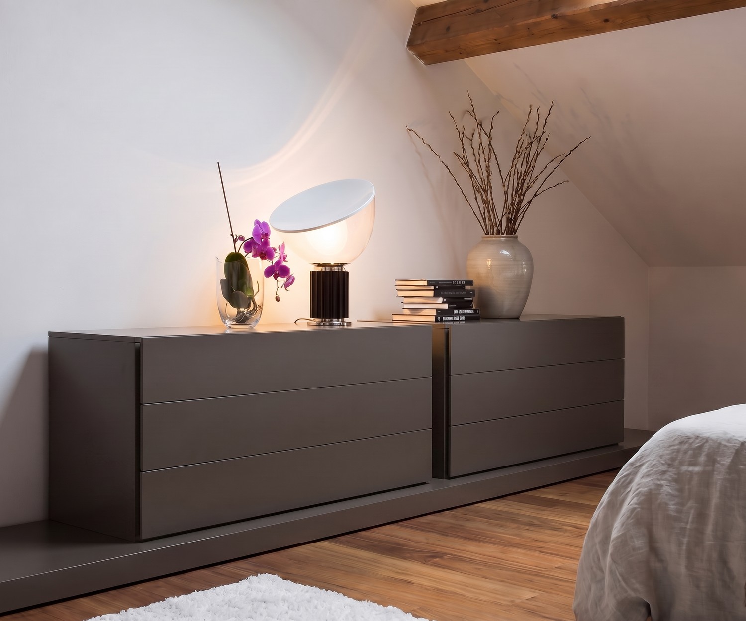 Novamobili Easy ladekast met 3 laden in de slaapkamer, modern grijs design onder schuin dak met sfeervolle tafellamp.