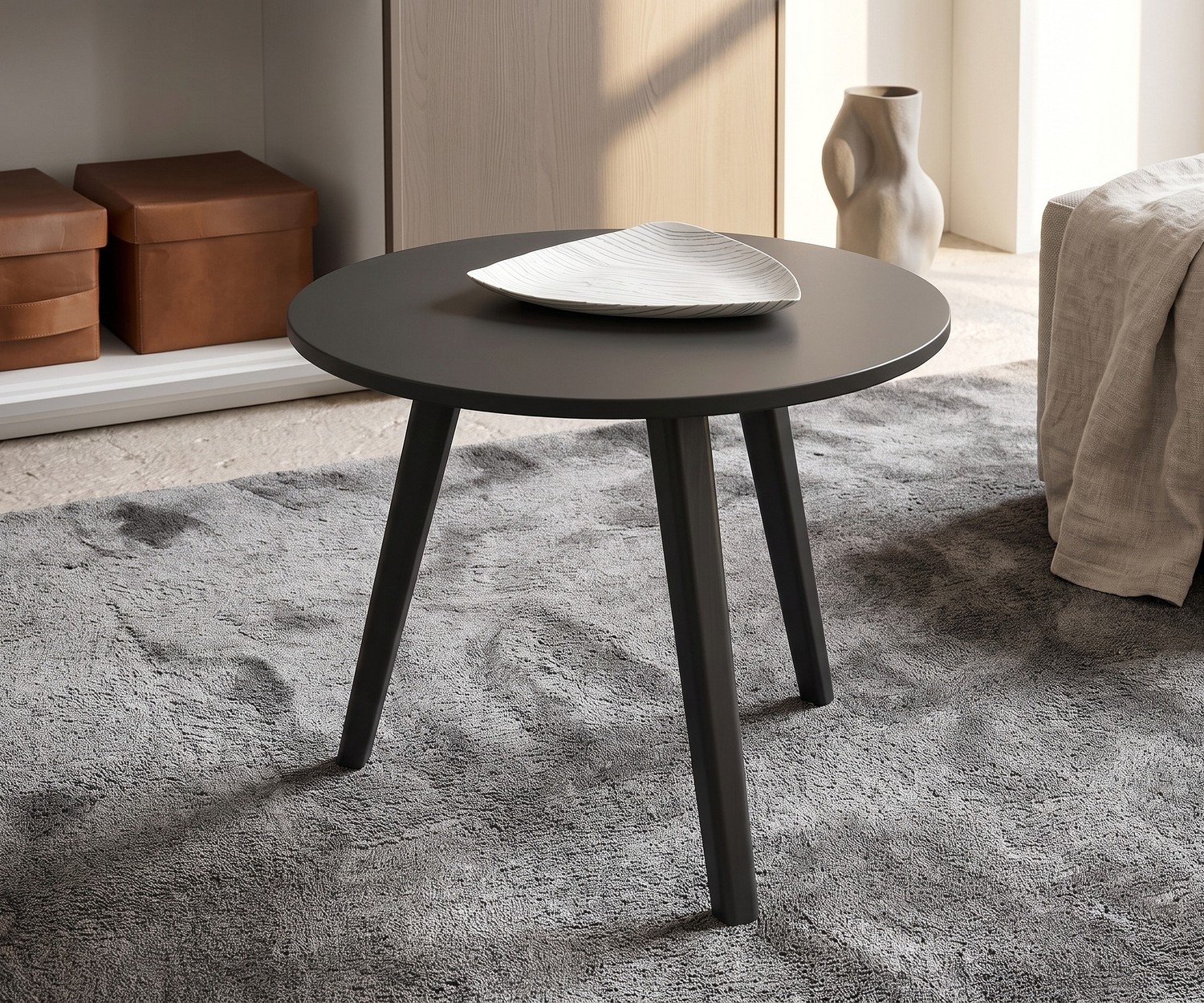 Woonkamer bijzetter Trio van Novamobili. Ronde donkergrijze design salontafel met drie houten poten op een grijs tapijt.