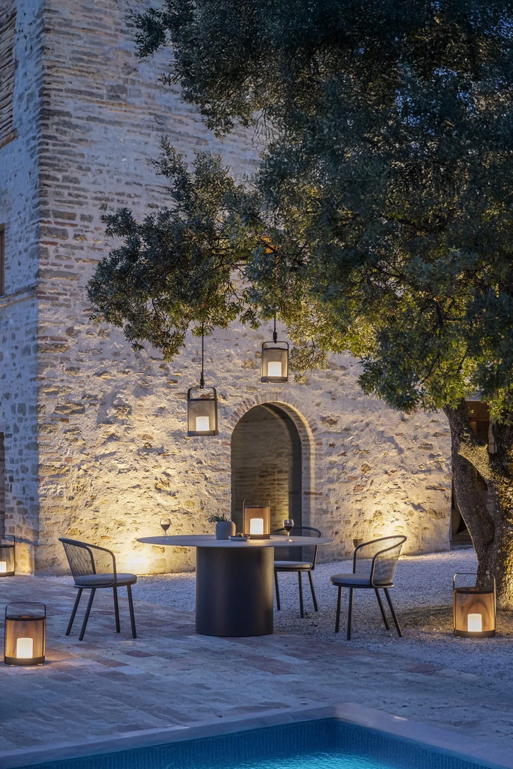 sfeervol-verlicht-terras-met-moderne-tafel-van-roestvrij-staal-en-keramiek-en-tuinstoelen-van-roestvrij-staal