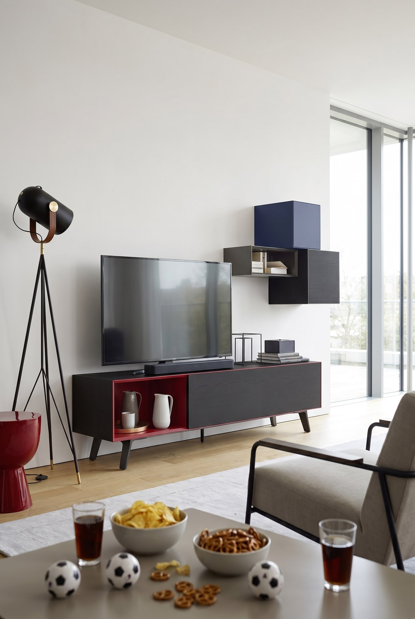 Reduziertes Wohnzimmer mit mattweißem Lowboard, einem großen Fernseher und einer kompakten Soundbar davor